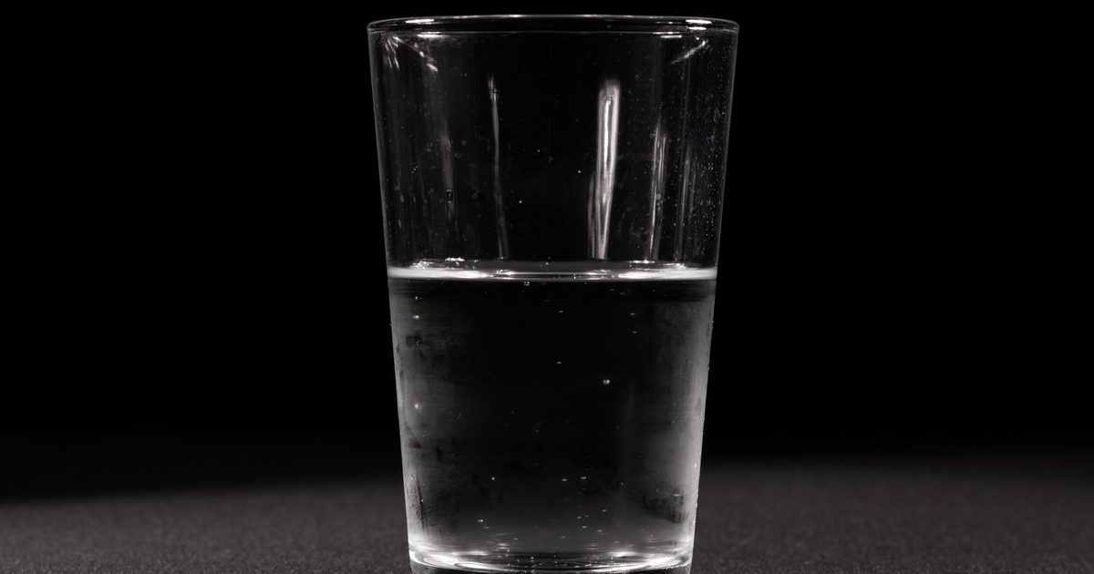 Vaso de agua lleno hasta la mitad sobre un fondo oscuro.