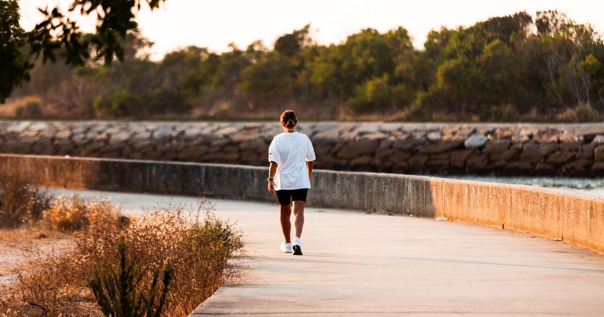 Persona caminando por un paseo junto al mar al atardecer.