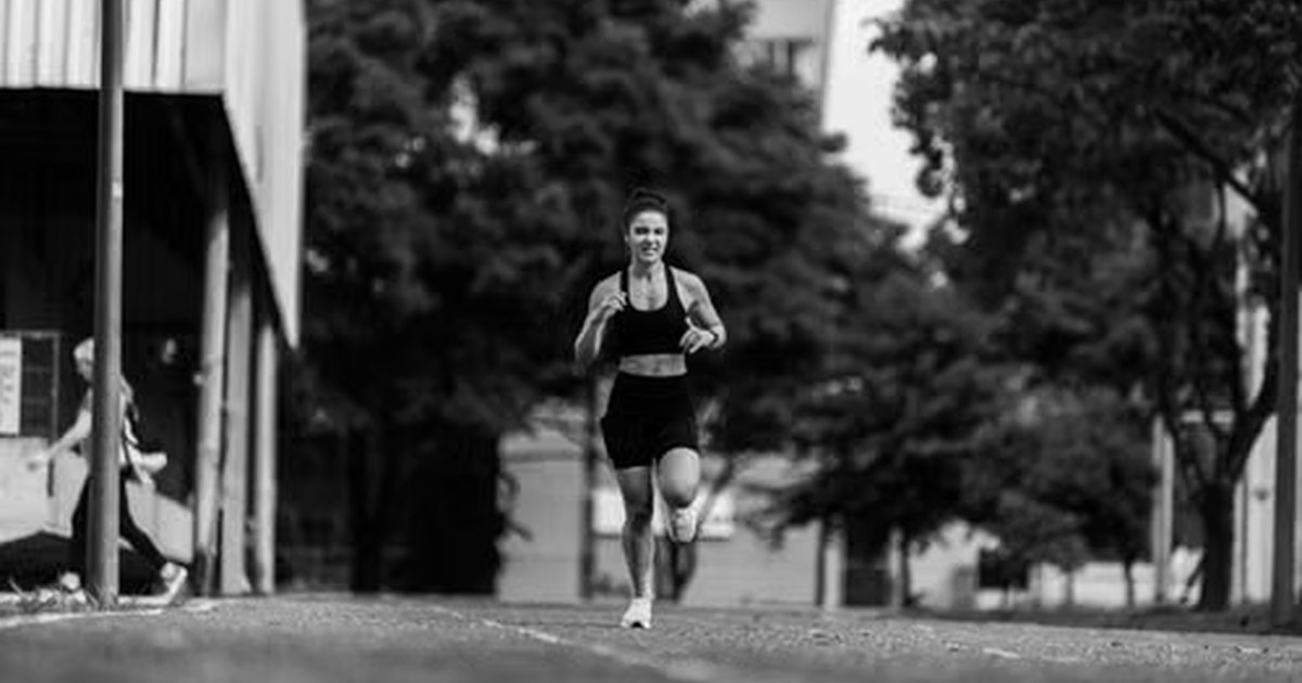 Mujer corriendo por una calle arbolada, en fotografía en blanco y negro.