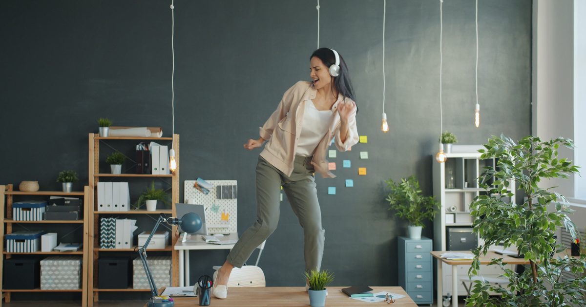 Mujer con auriculares bailando sobre un escritorio de oficina durante una pausa activa.
